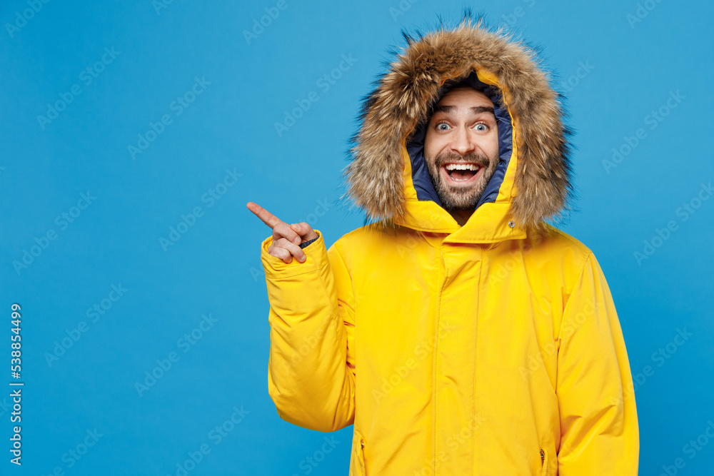Young man 20s wear yellow puffer down jacket with fur hood point index finger aside on