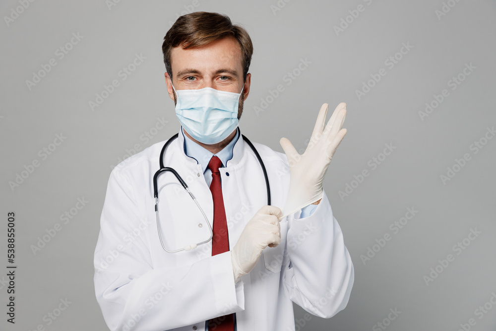 Male doctor man wears white medical gown suit sterile disposable protective face mask gloves look camera work in hospital isolated on plain grey color background studio. Healthcare medicine concept.