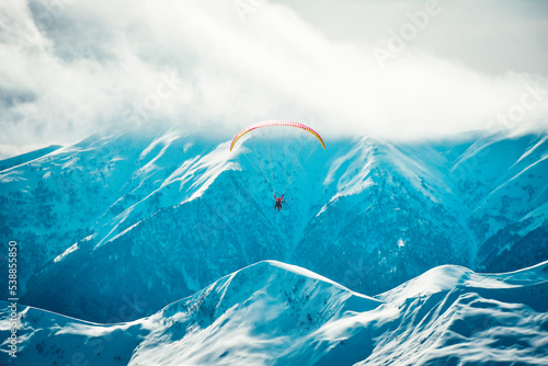Fototapeta Naklejka Na Ścianę i Meble -  People paragliding tandem above mountain in winter in Georgia ski resort. Concept of active lifestyle and extreme sport adventure.
