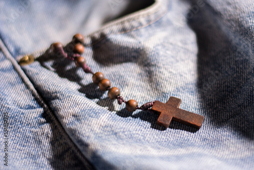 Fototapeta wooden brown cross with rosary crown on jeans color background