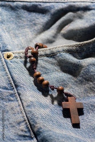 wooden brown cross with rosary crown on jeans color background