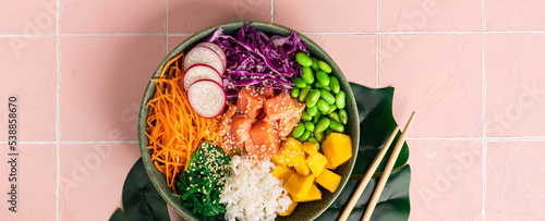 Poke-a bowl with fresh salmon, rice, chuka salad, edamame beans, carrots and red cabbage. Healthy food bowl on pink background, top view. Banner