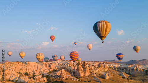 Hot air balloons under rocky landscape of natural formations at sunrise in Cappadocia, central Turkey.