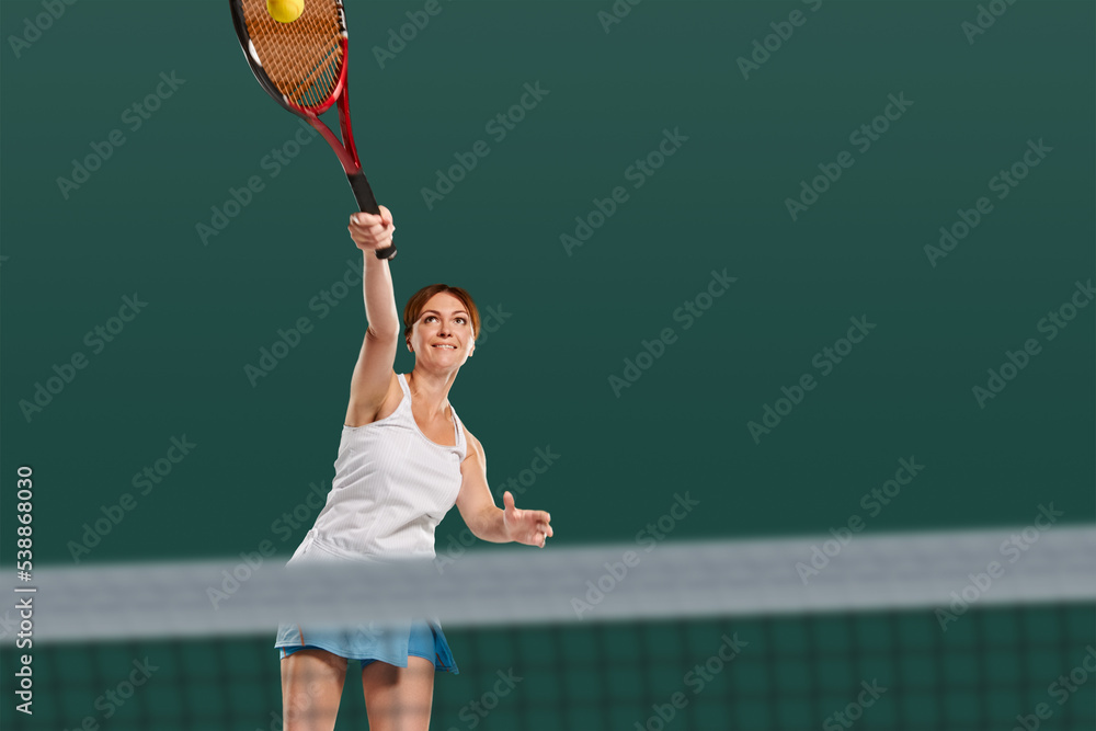 Portrait of beautiful sporty girl in white uniform serving ball during tennis game