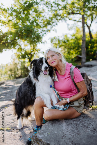 Senior woman resting and stroking her dog during walking in forest.