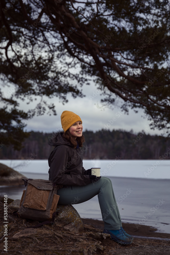woman sitting on a rock by a frozen lake in a forest woman sitting on a rock by a frozen lake in a forest