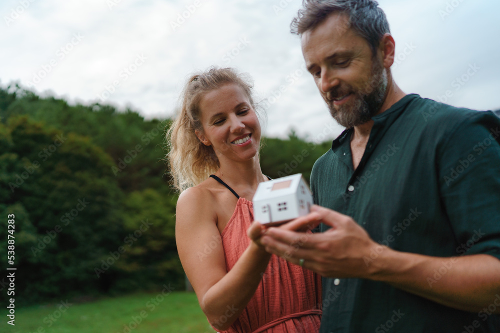 Close up of happy couple holding paper model of house with solar panels, looking and dreaming about future. Alternative energy, saving resources and sustainable lifestyle concept. Close up of happy couple holding paper model of house with solar panels, looking and dreaming about future. Alternative energy, saving resources and sustainable lifestyle concept.