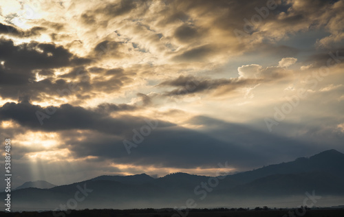 Dramatic cloudy sky and sun rays during a beautiful autumn morning on top of the mountains.