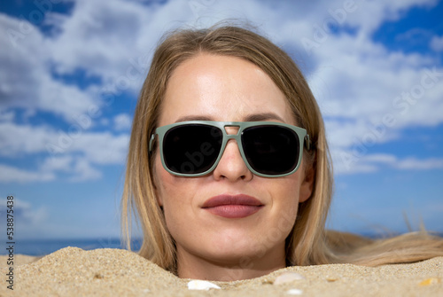 Woman buried in sand on beach with sunglasses © Dan Talson