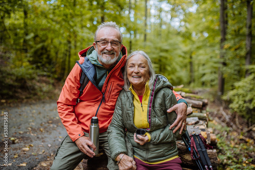 Senior couple having break during hiking in autumn forest.