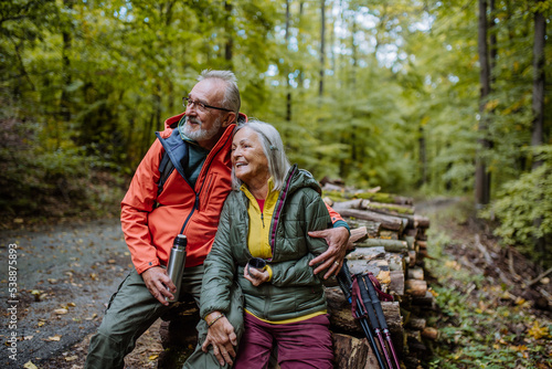 Senior couple having break during hiking in autumn forest.