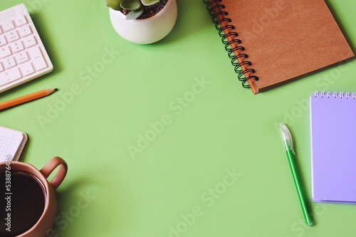 Modern office table top view photo. Items on a green desk. Computer keyboard, diary, pen, cactus and cup of coffee. Mockup, free space for text