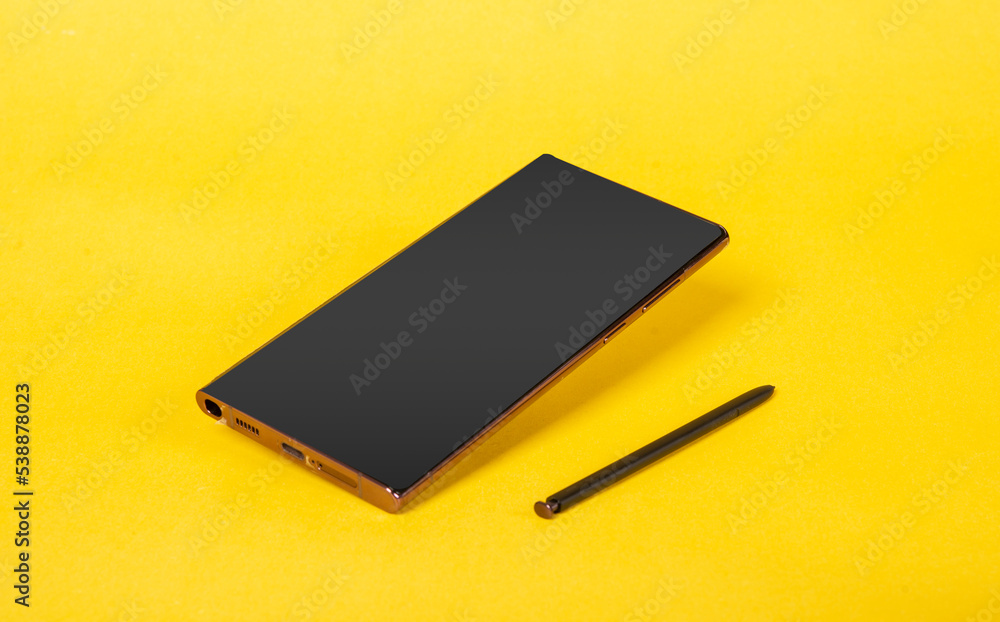Modern Smartphone with touch pen isolated on yellow banner Modern Smartphone with touch pen isolated on yellow banner