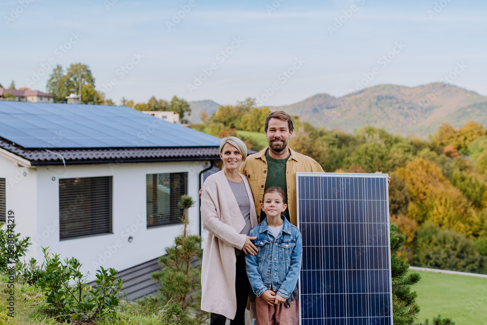 Happy family near their house with solar panel. Alternative energy, saving resources and sustainable lifestyle concept.