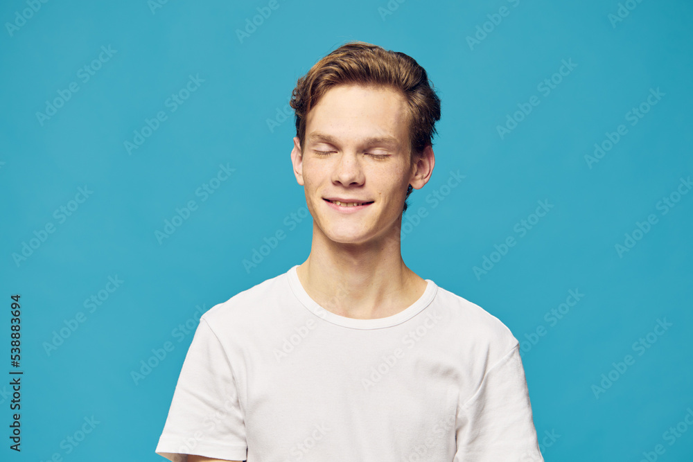 portrait of a guy in a white T-shirt with closed eyes on a blue background portrait of a guy in a white T-shirt with closed eyes on a blue background