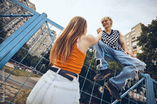 A teenage boy is helping his female friend to climb up the fence.