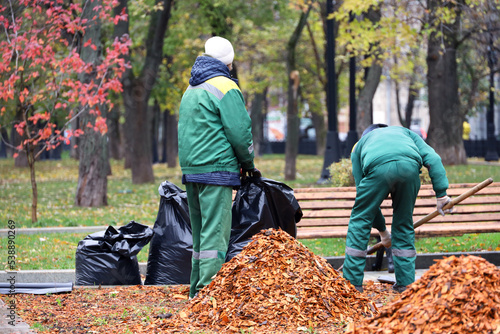 Two workers clean the lawns in autumn park. City improvement, man and woman janitors with shovel and garbage bags