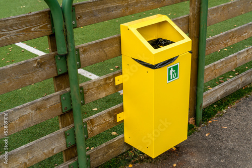 Yellow garbage bin hanging on the fence