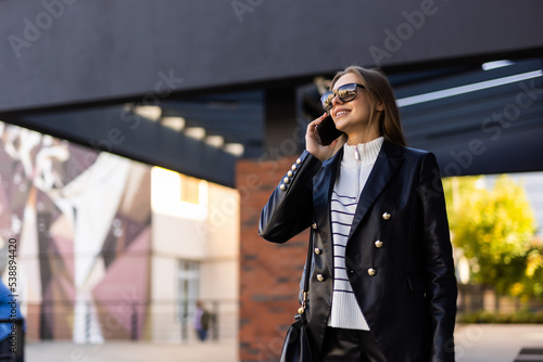 Portrait of young woman talking on the phone while standing outdoors at the street. Business concept.