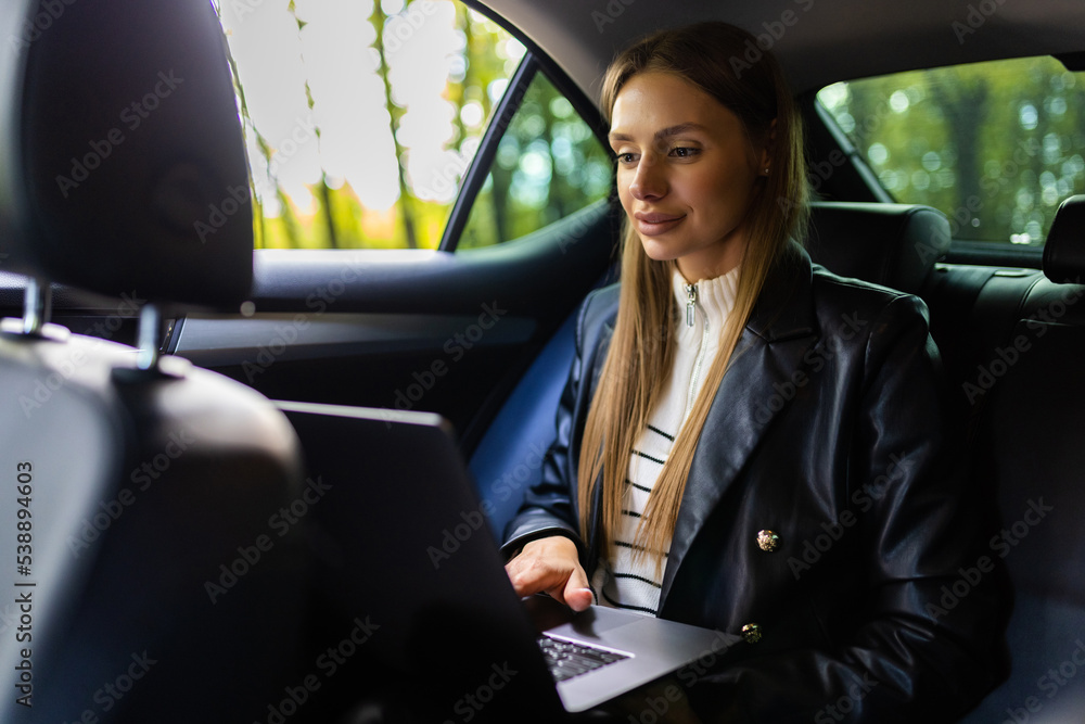 Beautiful young business woman is using laptop in the car