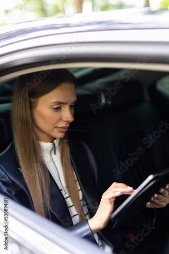 Young, woman sitting in the back seat of a car with a tablet in hands
