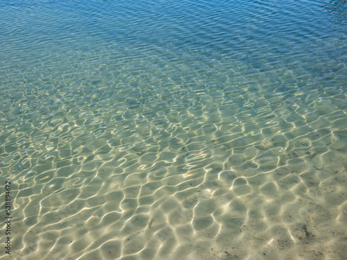 Texture of beautiful  crystal clear light blue and turquoise transparent water with fine white sand base with bright reflection of sun in water movement