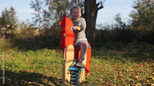 A little girl is swinging on a toy horse, a child is playing in the yard on the playground photo