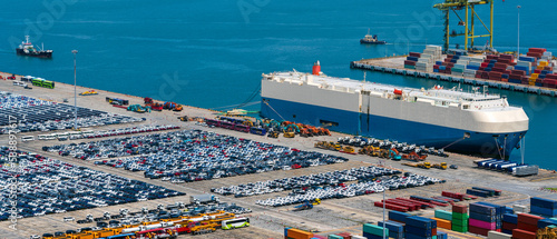 Canvas Print Lined up imported cars with car carrier ship anchored at the terminal