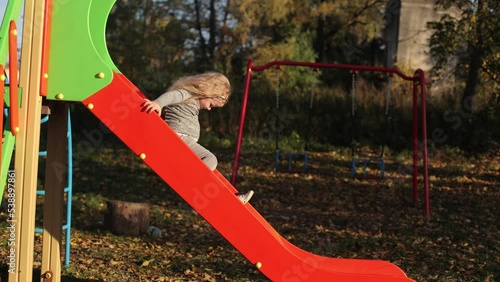 The child plays in the yard on the playground, rides on the slide, the girl is in a great mood, cheerful photo