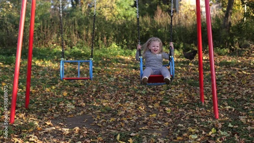 The child plays in the yard on the playground, rides on the swing, the girl is in a great mood, cheerful photo