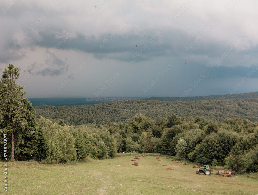 Summer mountain landscape. Tractor picks up hay in the meadow. Carpathian Mountines, Ukraine, Eastern Europe.