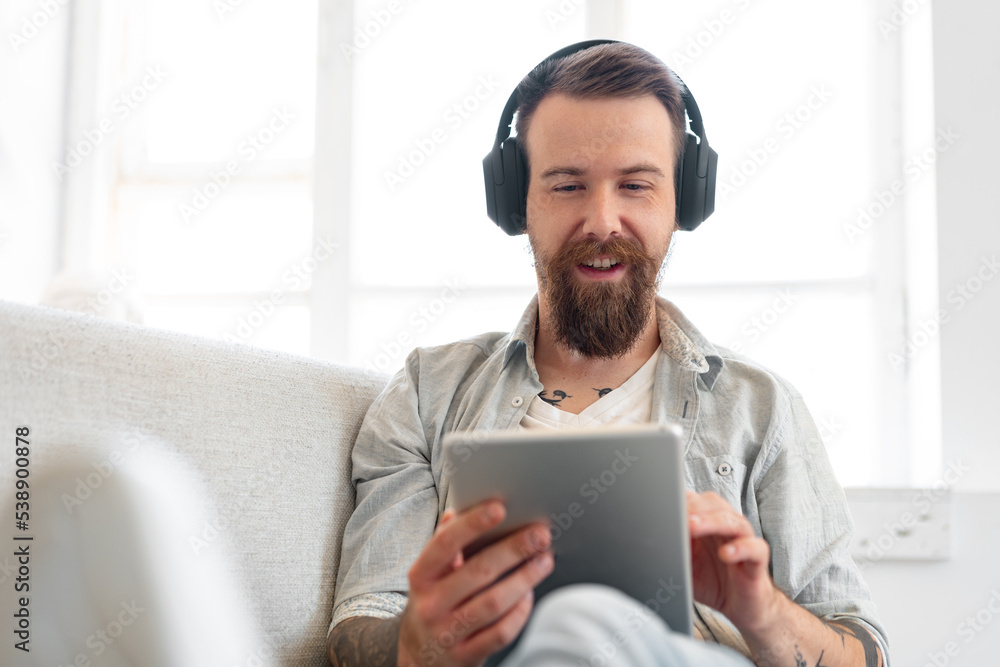 Handsome bearded man using digital tablet while resting on couch at home Handsome bearded man using digital tablet while resting on couch at home