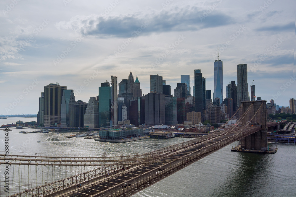 Manhattan in background along East River with picturesque Brooklyn Bridge New York City United States from panorama aerial view.