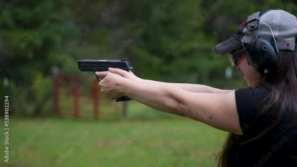 Young woman wearing ear protection fires handgun at a target outside on a summer day. Young woman wearing ear protection fires handgun at a target outside on a summer day.