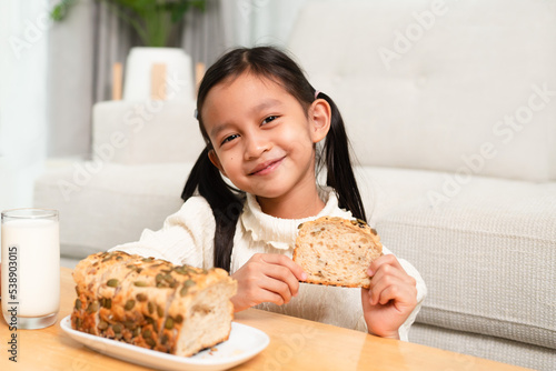Принти на полотні Asian little girl is eating multigrain whole whet homemade bread and drink milk with happy moment