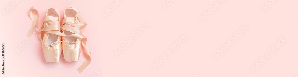 New pastel beige ballet shoes with satin ribbon isolated on pink background. Ballerina classical pointe shoes for dance training. Ballet school concept. Top view flat lay copy space banner New pastel beige ballet shoes with satin ribbon isolated on pink background. Ballerina classical pointe shoes for dance training. Ballet school concept. Top view flat lay copy space banner