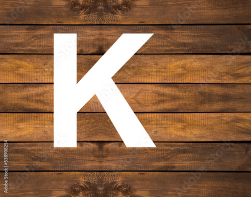 Alphabet letter K in white hole on wood background
