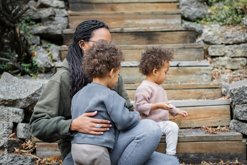 Black mother with her biracial twins on stairs in backyard in fall 