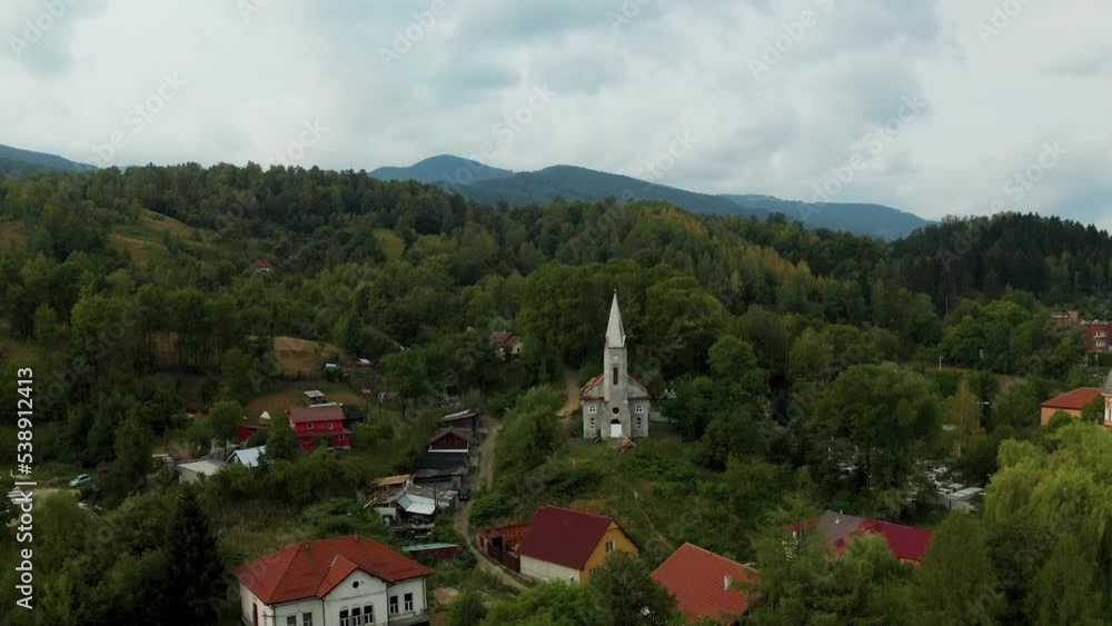 Aerial view of an old Romanian church located in a small town between the mountains and surrounded by dense forest. Town of Lupeni, in the region of Hunedoara. White facade churches drone view. Aerial view of an old Romanian church located in a small town between the mountains and surrounded by dense forest. Town of Lupeni, in the region of Hunedoara. White facade churches drone view.
