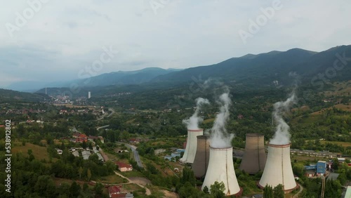 Aerial drone shot passing thru power plant chimneys, revealing mountains in the background. Paroșeni Power Station is a large electricity producer and one of the largest thermal power plants in the EU