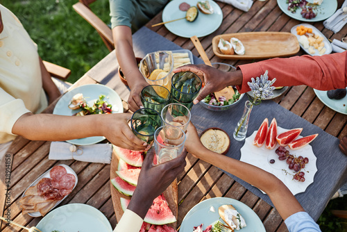 Top view at group of African American people clinking glasses over table with delicious food outdoors