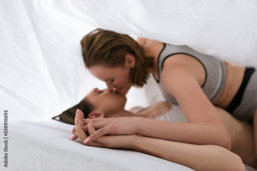blurred lesbians holding hands and kissing while lying under white blanket. blurred lesbians holding hands and kissing while lying under white blanket.