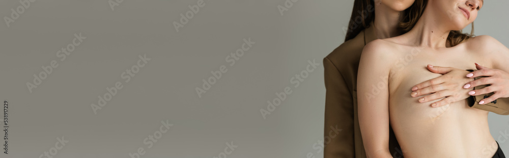 Fototapeta premium partial view of lesbian woman covering breast of young sensual girlfriend isolated on grey, banner.