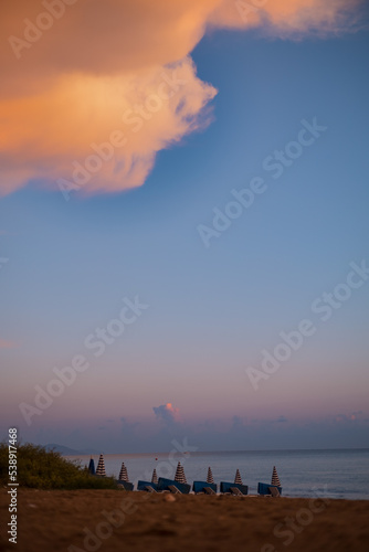 Calm landscape of seaside at sunset  closed sun umbrellas on the beach under sunset cloud