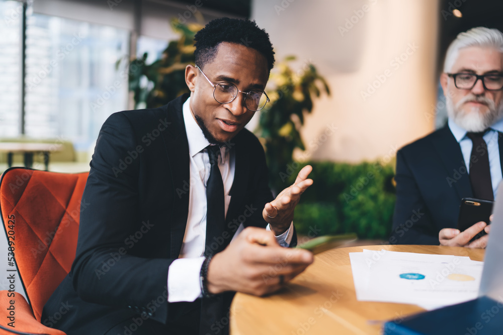 Black businessman using mobile phone during meeting in office Black businessman using mobile phone during meeting in office