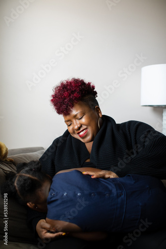African American mother tickles daughter on couch © Nadiya Nacorda