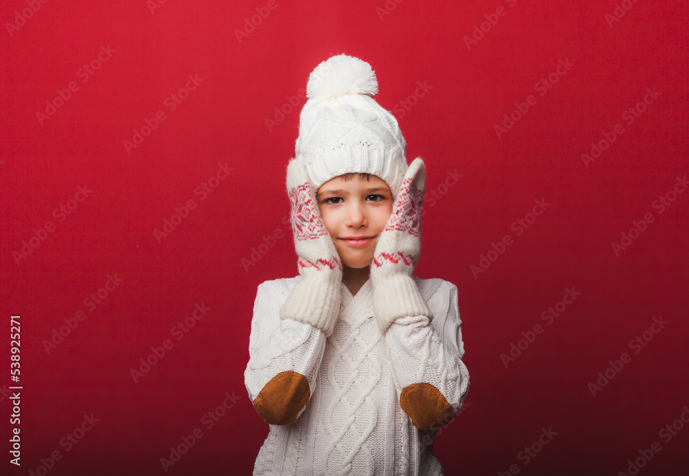 Winter portrait of a happy, joyful child-a boy in a knitted hat and sweater, having fun on a red background. the boy looks at his palms Winter portrait of a happy, joyful child-a boy in a knitted hat and sweater, having fun on a red background. the boy looks at his palms