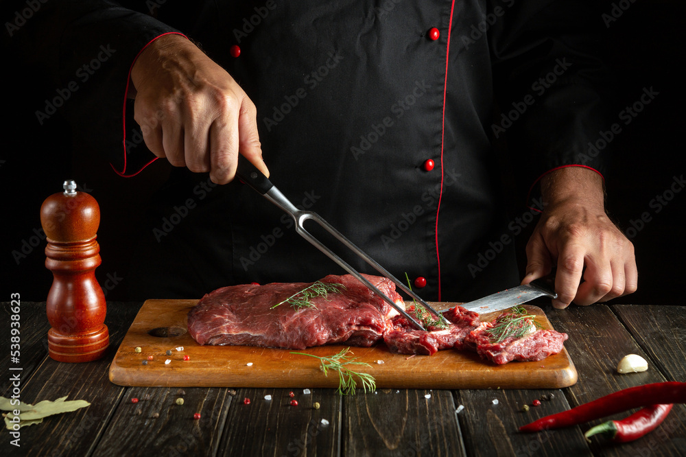 The chef prepares raw meat on a kitchen cutting board. Idea for a hotel menu on a dark background