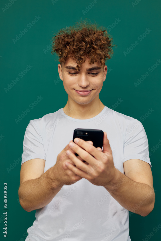 a funny, joyful man with curly hair stands against a green background and holds his smartphone with both hands, carefully looking into it. vertical photography in the studio a funny, joyful man with curly hair stands against a green background and holds his smartphone with both hands, carefully looking into it. vertical photography in the studio