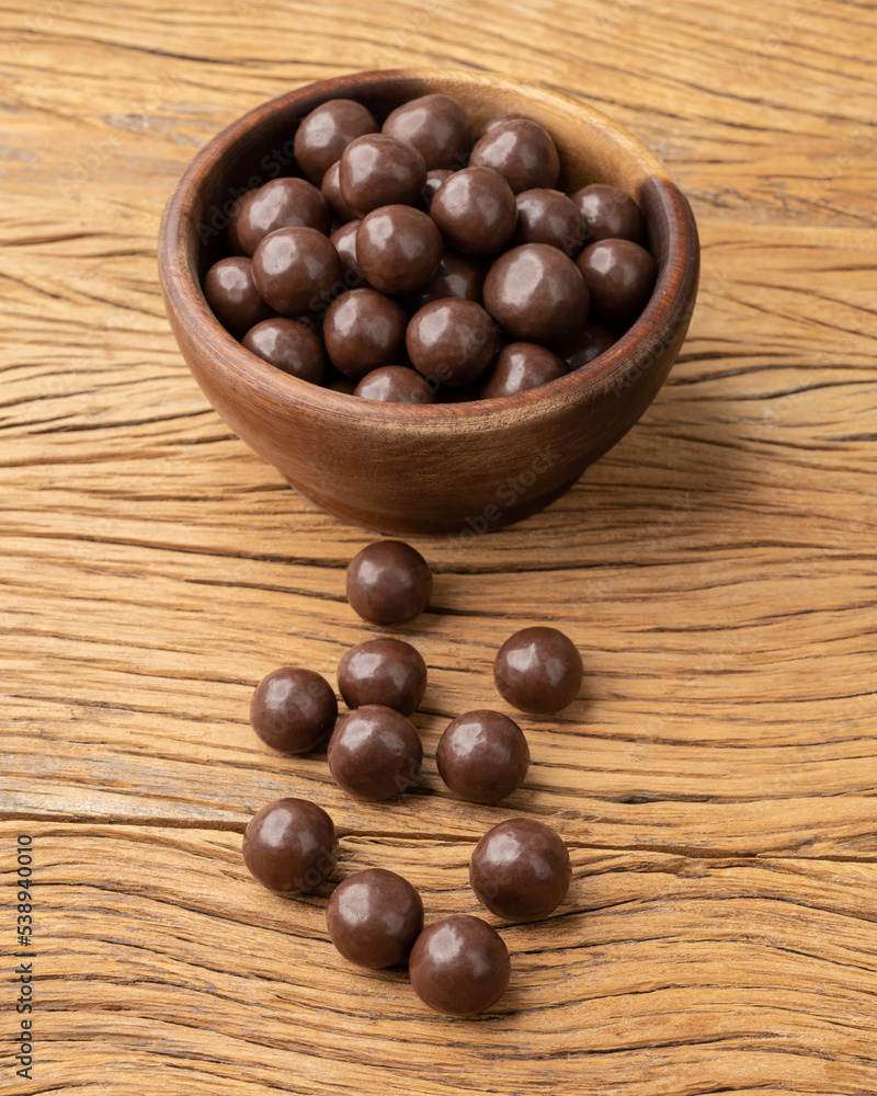 Obraz premium Chocolate malted balls on a bowl over wooden table